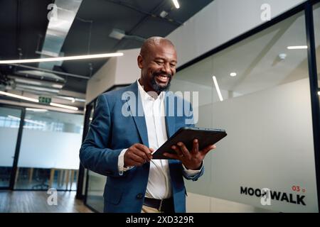 Mature black man in businesswear smiling with digital tablet in corridor of office Stock Photo