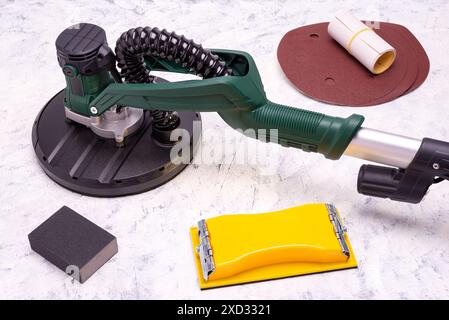 Tool for smoothing and sanding walls. Electric sander with telescopic handle, hand sander, black sand abrasive bar and sandpaper on grey-white backgro Stock Photo