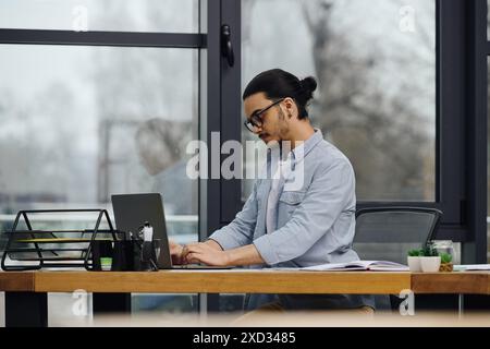 A man deeply focused on his laptop while seated at a desk. Stock Photo