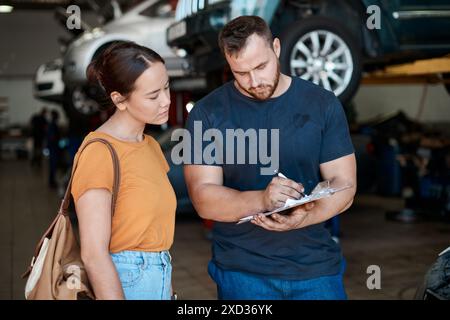 Woman, mechanic and sign paperwork in auto repair shop, invoice and service for car maintenance bill. Female person, clipboard and customer for Stock Photo