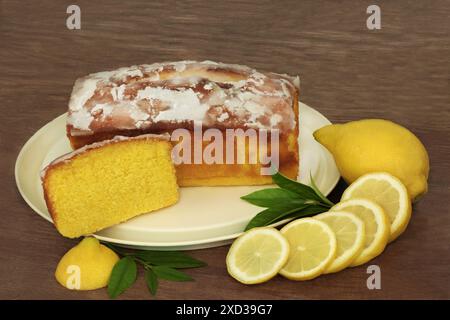 Lemon drizzle cake with slice, fresh fruit, leaves on rustic wood background. Homemade dessert for afternoon tea and celebratory events. Stock Photo