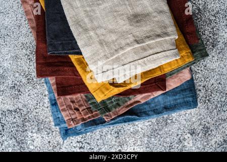 Top view of stacked textile napkins in various colors neatly arranged on a textured surface, showcasing a diverse palette and fabric textures. Stock Photo