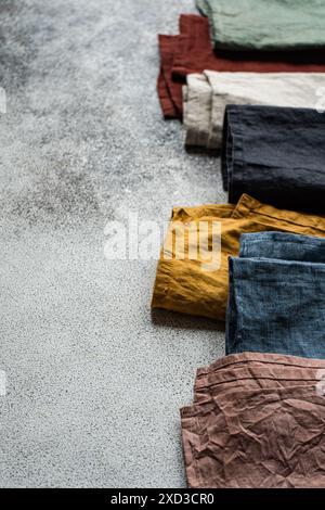 Top view of colorful textile napkins arrayed on a gray textured surface, showcasing a variety of fabric textures and folds in an elegant flat lay arra Stock Photo