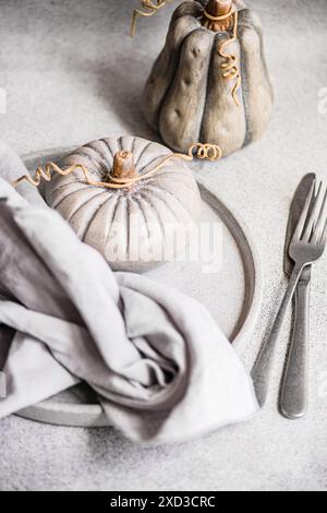 A stylish autumnal table arrangement featuring unique ceramic pumpkins, a draped linen napkin, and modern cutlery on a textured surface Stock Photo