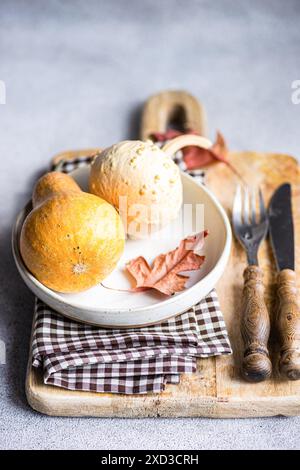 A cozy autumnal flat lay featuring gourds and a dried leaf on a rustic wooden board, accompanied by a checkered napkin and vintage cutlery Stock Photo