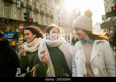 A joyful group likely of a family, with three women laughing and walking down a bustling London street. They are enjoying ice cream cones and basking Stock Photo