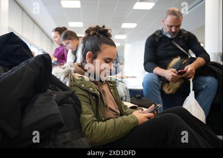 Side view of young woman and family members using smartphones while waiting in a public area. Stock Photo