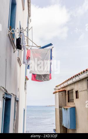 A charming coastal alleyway featuring laundry drying on a clothesline between two buildings. The narrow passage opens up to a stunning ocean view, cap Stock Photo