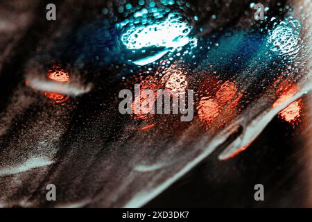 A captivating close-up photo showcasing the intense play of red and blue street lights reflecting on a rain-soaked surface, dotted with water droplets Stock Photo