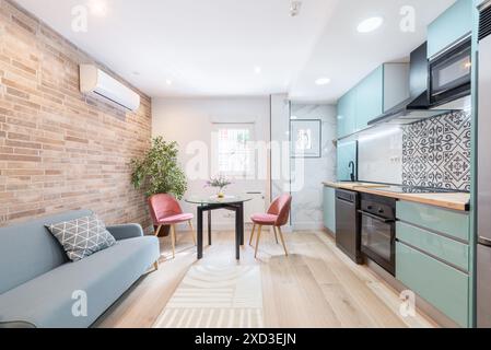 A beautifully arranged small apartment featuring exposed brick walls, a compact kitchen with blue cabinets, and a cozy sitting area. Accents of marble Stock Photo