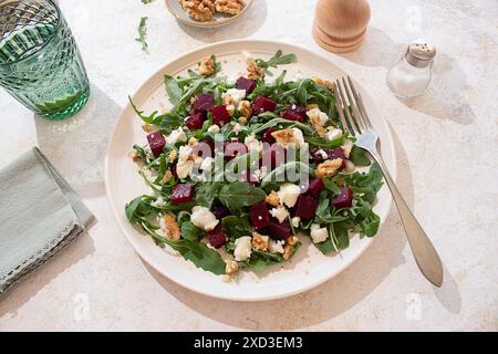 Healthy goat cheese, arugula and beetroot salad on a beige plate and styled with a pepper mill, a lime water glass on a rustic but vibrant atmosphere Stock Photo