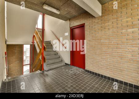 A red door in a brick wall with stairs leading up to the second floor and an open doorway on the right side Stock Photo