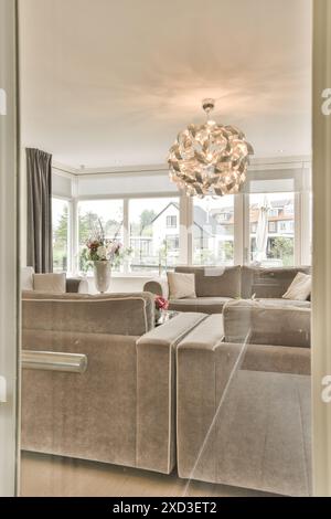 A living room with couches, chairs and a chandel in the center of the room is large windows Stock Photo