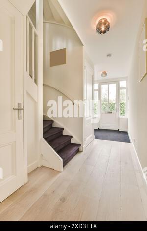 A hallway in a house with hardwood flooring and white walls, wooden stairs leading up to the front door Stock Photo