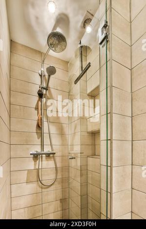 A contemporary shower stall featuring a sleek rainfall showerhead, a handheld shower, and beige tiled walls. The glass door and built-in shelving add Stock Photo