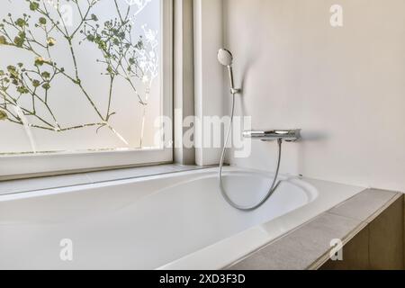 Bright and airy bathroom features a clean white bathtub and shower, elegantly complemented by a window adorned with tree motifs, creating a serene and Stock Photo