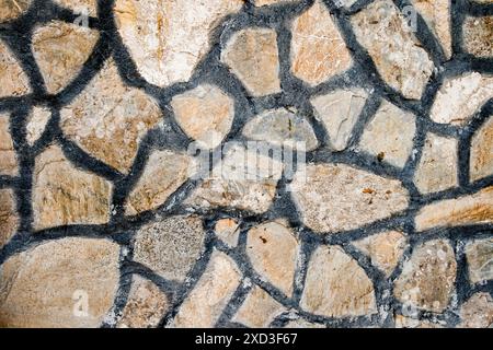 Close up of a stone wall with irregularly shaped stones and dark mortar lines, texture, background. Stock Photo