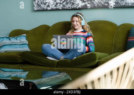 A young woman enjoys remote working from her comfortable home, equipped with headphones and a laptop, embracing the smart working lifestyle Stock Photo