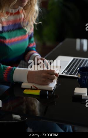 Anonymous young woman enjoys working from home, writing in a notebook a cozy remote office setup highlighting smart work flexibility Stock Photo