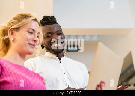 Diverse man and woman sharing a cheerful moment while viewing content on a laptop in a well-lit office space They show genuine smiles and teamwork Stock Photo