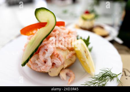 A delicious shrimp salad sandwich garnished with cucumber, bell pepper, and lemon, served on a white plate. Stock Photo
