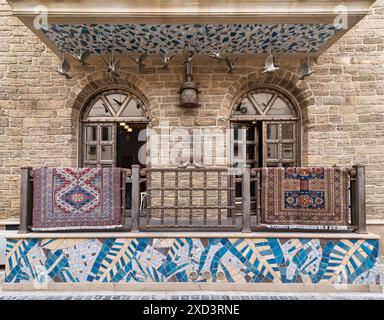 A view of a building in Old Town Baku, Azerbaijan. The balcony has a tiled roof and iron railings. Two decorative rugs hang on the railing, adding a splash of color to the scene Stock Photo