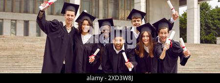 Portrait of a group of laughing happy multiracial graduates holding diploma outdoor. Stock Photo