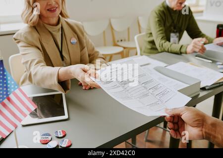 High angle view of mature woman working at polling station giving ballot paper to unrecognizable voter Stock Photo