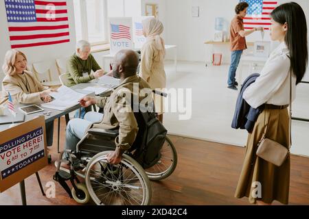 High angle view shot of Black man in wheelchair and ethnically diverse young people taking ballot papers and voting at polling station Stock Photo