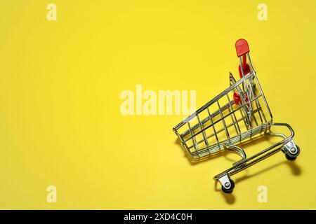 Flat lay image of red shopping cart on a yellow background with copy space. Consumerism and shopping concept. Stock Photo