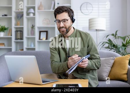 Professional man working from home during an online meeting with a headset and laptop in a cozy living room. Stock Photo