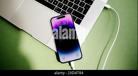 Paris, France - Sep 29, 2022: An iPhone 15 Pro connected to a MacBook Pro using a USB-C cable, showing a gradient purple and blue screen, illustrating the transition from Lightning port to USB-C on the latest iPhone model Stock Photo