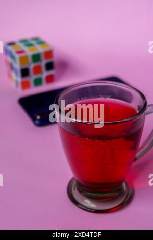 Photo of red drink, blue smartphone and Rubik on a pink background Stock Photo
