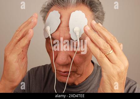 An elderly man using electrode pads on his forehead for pain relief or therapy. Stock Photo