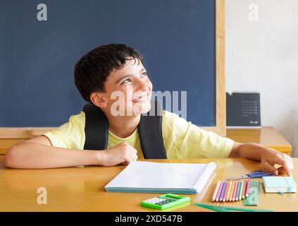 preteen boy happy and hopeful about going back to school with school supplies and slate and calendar in background Stock Photo