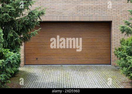 Wooden garage door closed, surrounded by brick wall and green pine trees. Stock Photo