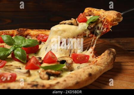 Taking piece of tasty pizza with melted cheese at wooden table, closeup Stock Photo