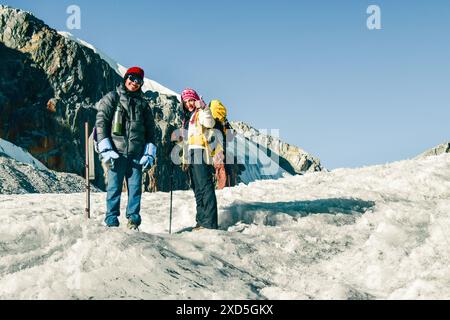 Two trekkers on trek stand on glacier looking at camera. Chola glacier pass in Himalayas. Nepalese male guide leading tourist client in Sagarmatha nat Stock Photo