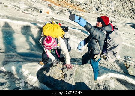 Two trekkers trekking in Himalayas mountains through Chola glacier pass to Gokyo Ri. Nepalese male guide leading tourist client in Sagarmatha national Stock Photo