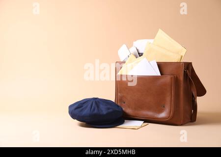Brown postman's bag, envelopes, newspapers and hat on beige background. Space for text Stock Photo