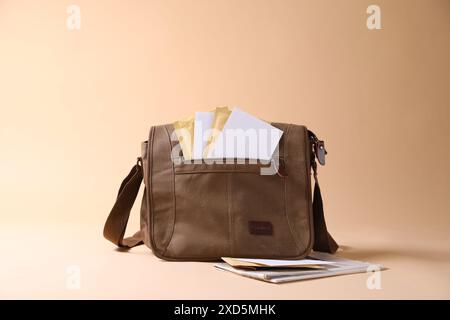 Brown postman's bag with envelopes and newspapers on beige background Stock Photo