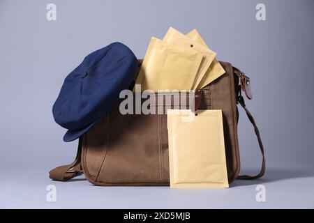Brown postman's bag, envelopes, newspapers and hat on grey background Stock Photo