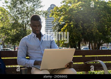 Concentrated African American executive, working outdoors with his laptop and a cup of coffee. Concept of remote work, business and enjoying natural e Stock Photo