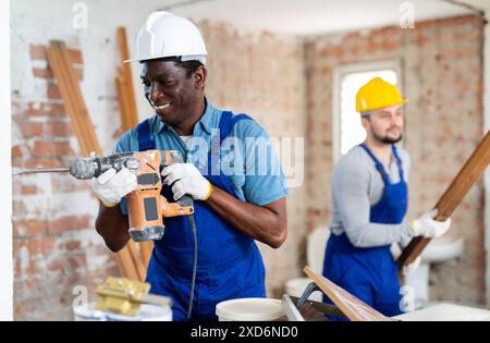 African-american man builder using demolition hammer on wall in apartment Stock Photo