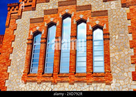 Old red brick building with narrow windows and blue sky in the background. Showcasing architectural grandeur and the passage of time. Stock Photo