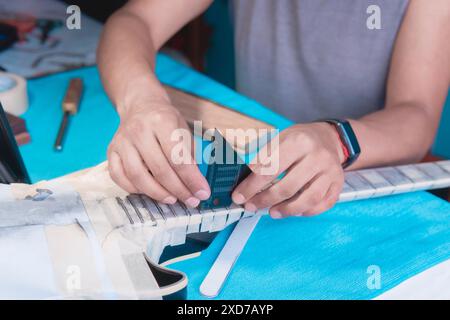 Black electric guitar in repair shop with hands of guitar luthier fixing it, Guitar technician aligns frets on electric guitar neck with leveling bar. Stock Photo