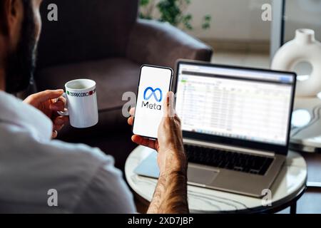 Man holding a smartphone showing Meta logo on mobile phone screen. Laptop with Facebook business manager on background. Rosario, Argentina - June 20, Stock Photo