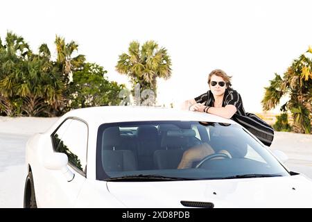 Young man in sunglasses leaning on the roof of a white car, posi Stock Photo