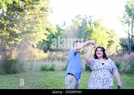 Happy pregnant woman dancing with her partner in a sunny, green Stock Photo