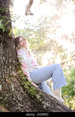 Trendy young woman with wavy blonde hair sitting on a tree trunk Stock Photo